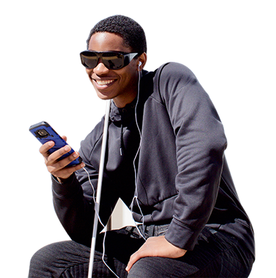 A young blind man wearing ear buds, listens to NFB-NEWSLINE on his phone outside.